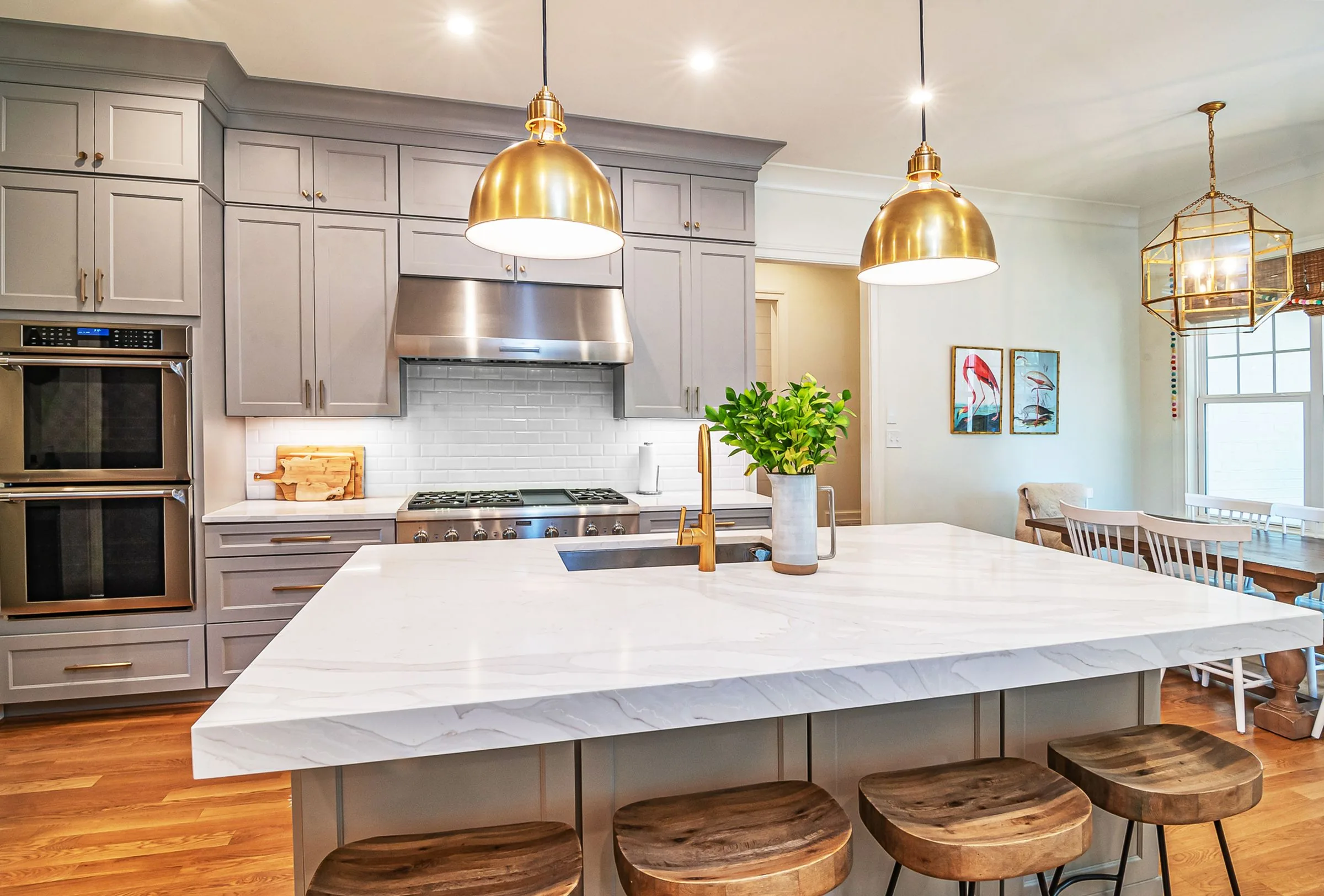 Modern kitchen with white marble island, gray cabinetry, stainless steel appliances, and brass pendant lights.
